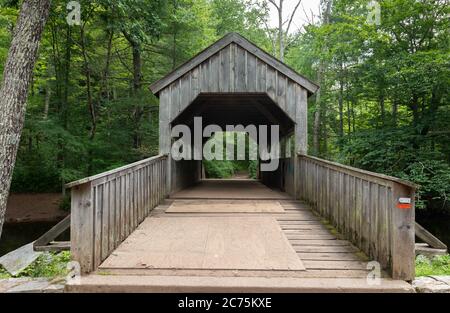 Hölzerne überdachte Brücke über einen kleinen Fluss in einem üppigen grünen Wald am Devil`s Hopyard State Park, Connecticut Stockfoto